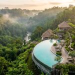 The Best Hotels in Ubud, Bali: 2025 Expert Guide An aerial view of a luxurious resort infinity pool overlooking a dense, vibrant green jungle valley in Ubud, Bali, at sunrise.