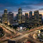 Why Visit Jakarta: Top Reasons to Explore Indonesia's Capital A vibrant, bustling wide shot of Jakarta's modern cityscape at dusk, featuring prominent skyscrapers illuminated against a colorful sky, with a hint of busy street life below, inviting travelers to discover the city.