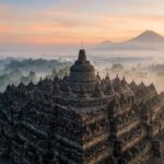 A wide shot of Borobudur Temple at sunrise with Mount Merapi in the background.