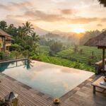 Best Accommodation in Ubud, Bali: Villas, Guesthouses & Boutique Stays A luxurious private villa with an infinity pool overlooking lush green rice terraces and palm trees in Ubud, Bali, at sunrise.