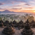 Things to Do on Java Island: A Complete 2025 Travel Guide A wide panoramic view of Borobudur Temple at sunrise, with mist rising from the jungle and volcanoes in the distance under a warm, golden sky.