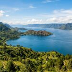 Visiting Lake Toba: 5 Essential Tips for 2025 | Travel Guide A wide view of Lake Toba with Samosir Island in the distance, surrounded by lush green hills.