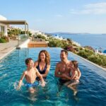 Best Luxury Family Hotels in Greece With Pool & Spa (2025) A family enjoying a large private pool overlooking the Aegean Sea at a luxury resort in Greece.