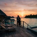 A couple relaxing on a private overwater bungalow deck at sunset.