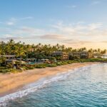 A wide view of the Four Seasons Resort Maui at Wailea from the beach, with palm trees and ocean.