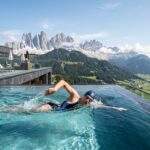 Luxury Alpin Panorama Hotel Hubertus: Full South Tyrol Guide (2025) A person swimming in an infinity pool overlooking a mountain valley.
