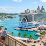 A modern Royal Caribbean cruise ship docked at a Caribbean port, with passengers enjoying a sunny day on deck.