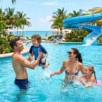 A family with two children playing in a resort swimming pool with a water slide.