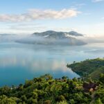 Top 5 Hotels in Lake Toba (2025): Best Stays by the Lake A serene overview of Lake Toba with Samosir Island in the distance under a clear sky.