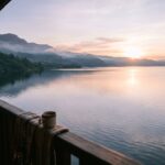 A serene sunrise over the expansive waters of Lake Toba, with distant hills.
